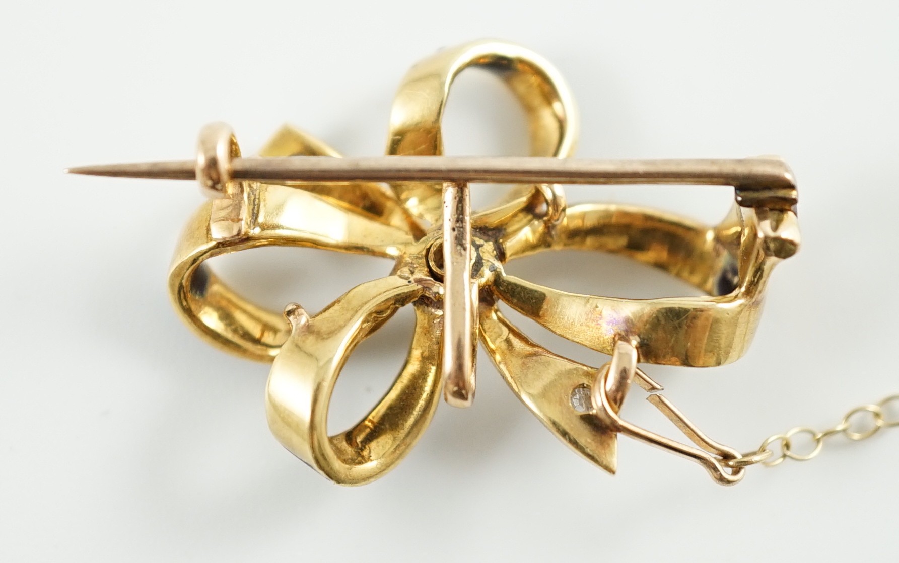 An early to mid 20th century gold, enamel and three stone diamond set ribbon bow brooch